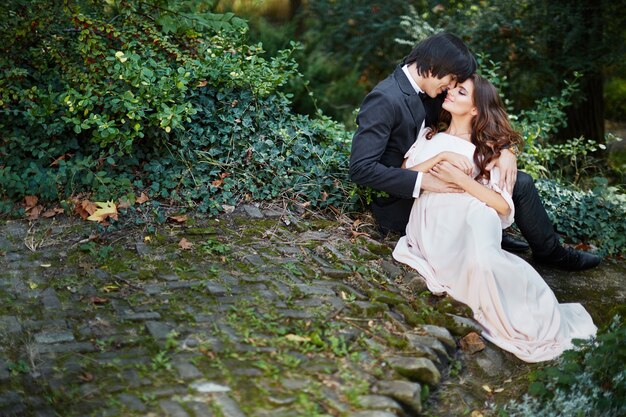 Bella sposa con lunghi capelli ricci e sposo seduto vicino a vicenda a foglie verdi, foto del matrimonio, bella coppia, giorno del matrimonio, ritratto.