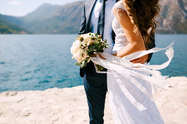 Bella sposa e sposo che abbracciano sulla costa la sposa tiene un mazzo di fiori