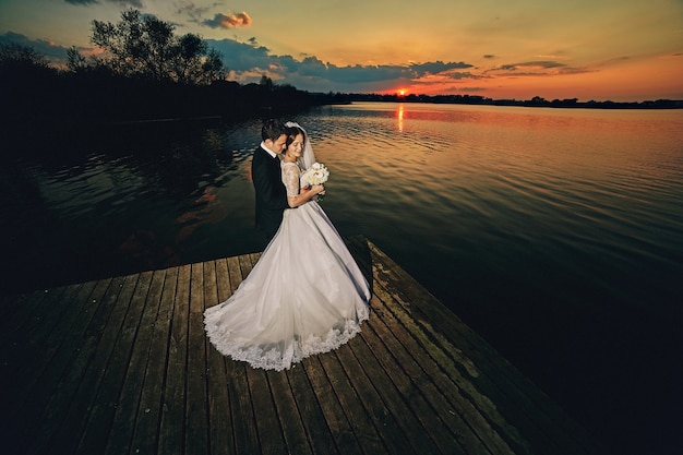 Bella sposa e sposo in posa vicino al lago al tramonto