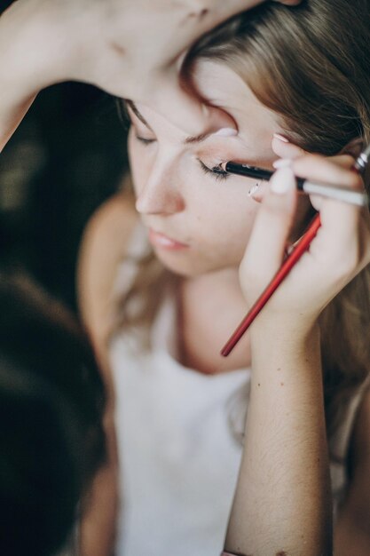 Bella sposa felice che si fa truccare da un truccatore professionista nella camera d'albergo Preparazione mattutina prima della cerimonia nuziale Stilista che applica gli ombretti