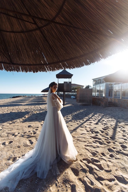 Bella sposa in abito bianco al sole cammina lungo la spiaggia di sabbia Elegante sposa al sole