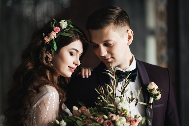 Bella sposa in abito bianco con bouquet di sposa e sposo bello in piedi e abbracciati