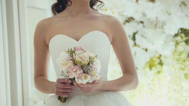 Bella sposa in abito da sposa con fiori in uno studio