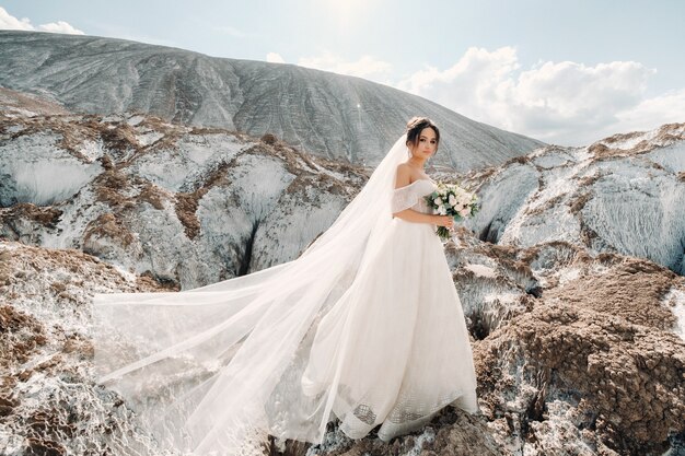 Bella sposa in abito da sposa con un bouquet in cima alle montagne di sale. Una splendida giovane sposa con i capelli ricci. Giorno del matrimonio. . Bellissimo ritratto della sposa senza lo sposo.