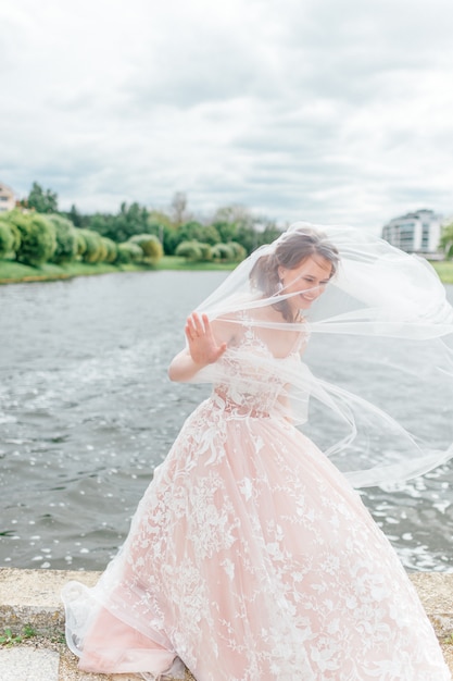 Bella sposa in abito da sposa con velo sul viso in posa all'aperto con il lago sullo sfondo