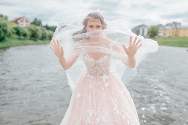 Bella sposa in abito da sposa con velo sul viso in posa all'aperto con il lago