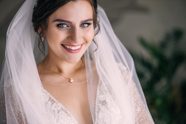 Bella sposa in posa in un abito da sposa e velo a casa Bel trucco e sorrisi