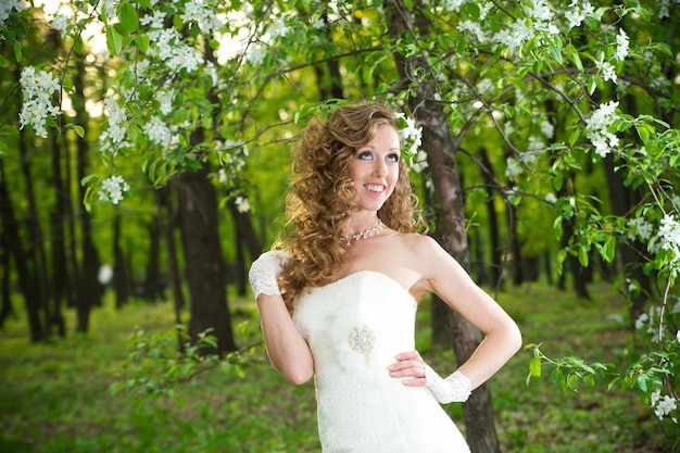 Bella sposa in un abito bianco in giardini fioriti in primavera Trucco e acconciatura professionali