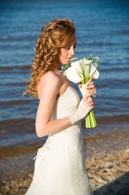 Bella sposa in un abito bianco sulla costa del fiume in estate