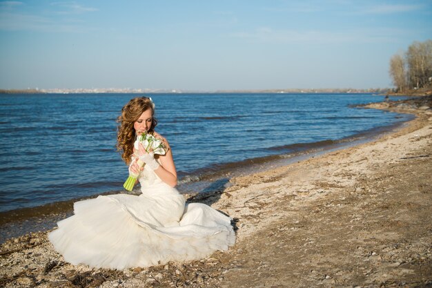 Bella sposa in un abito bianco sulla costa del fiume in estate