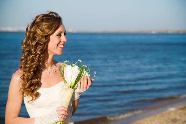 Bella sposa in un abito bianco sulla costa del fiume in estate