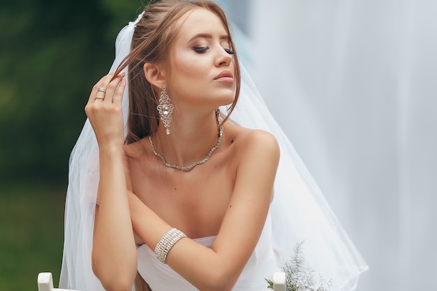 Bella sposa in un magnifico abito da sposa in posa tra il verde per strada. la ragazza posa in un abito da sposa per la pubblicità. Concetto di sposa per abiti pubblicitari.