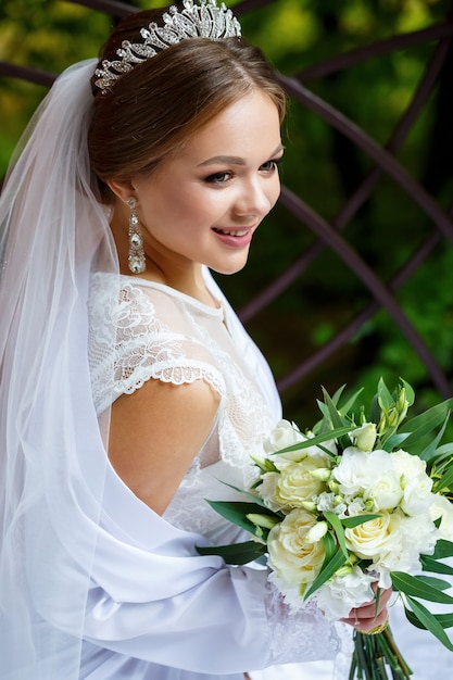 Bella sposa in velo e camice bianco si siede su una coperta con un bouquet da sposa nelle sue mani