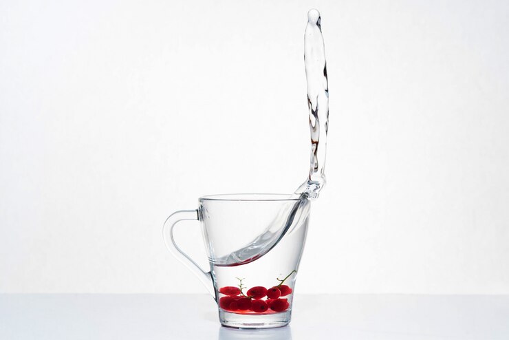 Bella spruzzata di acqua in una tazza di vetro con bacche sul fondo