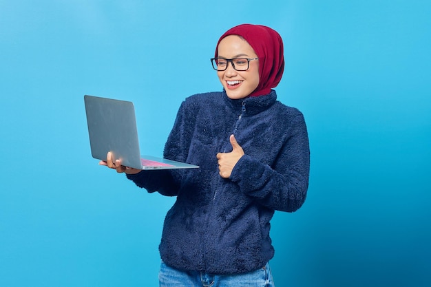 Bella studentessa asiatica che indossa una giacca blu che indossa un computer portatile e dà i pollici in su