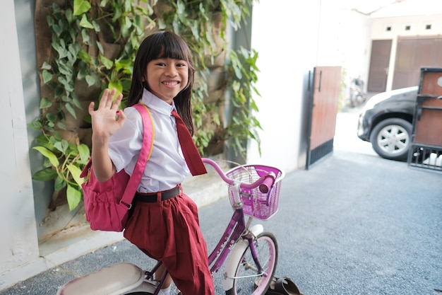 Bella studentessa asiatica delle elementari che va a scuola andando in bicicletta al mattino