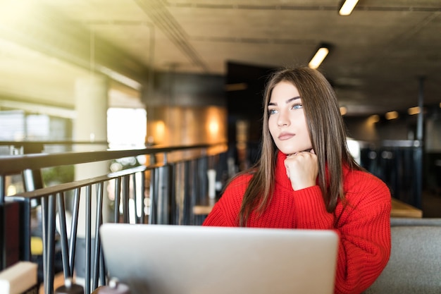 Bella studentessa con un sorriso carino che digita qualcosa sul net-book mentre si rilassa dopo le lezioni all'università