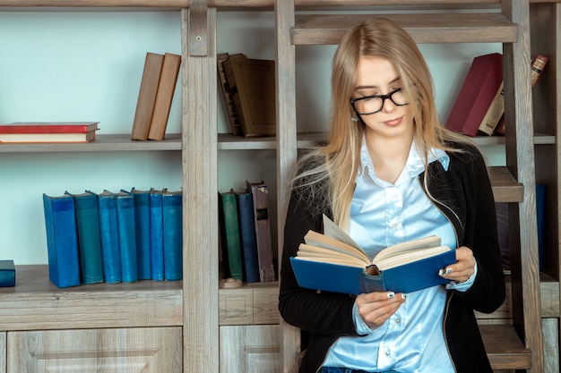 Bella studentessa in vetri che legge un libro vicino a una libreria