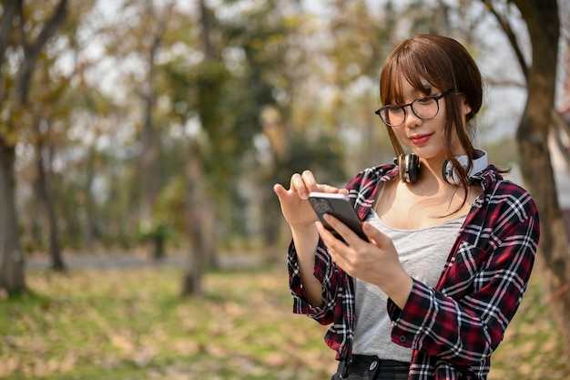 Bella studentessa universitaria asiatica che usa il suo telefono mentre si rilassa nel parco del campus