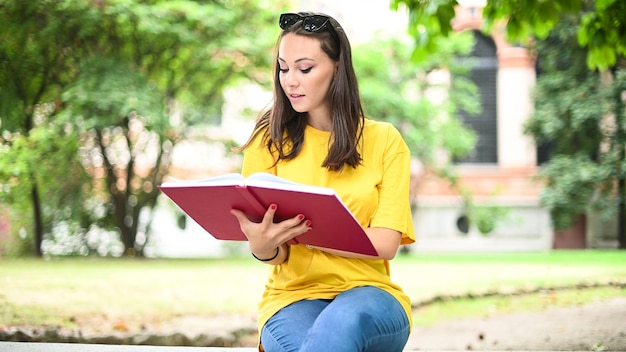Bella studentessa universitaria che legge un libro su una panchina in un parco
