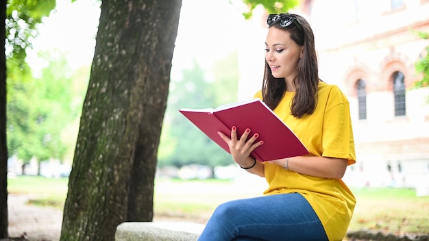 Bella studentessa universitaria che legge un libro su una panchina in un parco