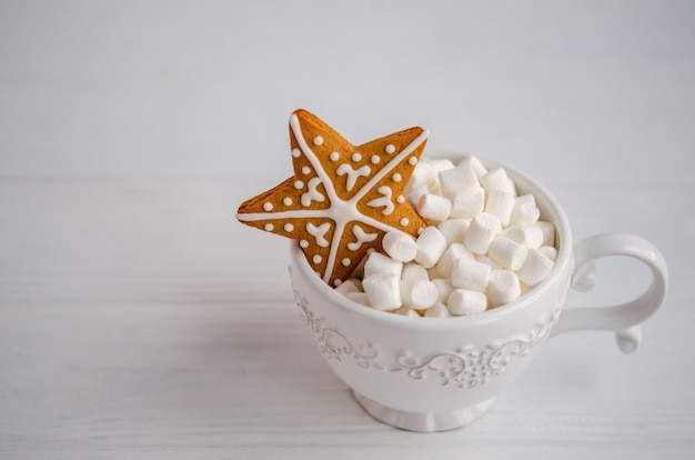 Bella tazza bianca con marshmallow bianchi all'interno e un pan di zenzero a forma di stella