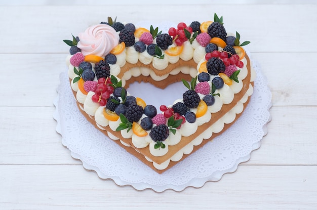 Bella torta a forma di cuore con frutti di bosco freschi per il giorno di San Valentino sulla tavola di legno bianca