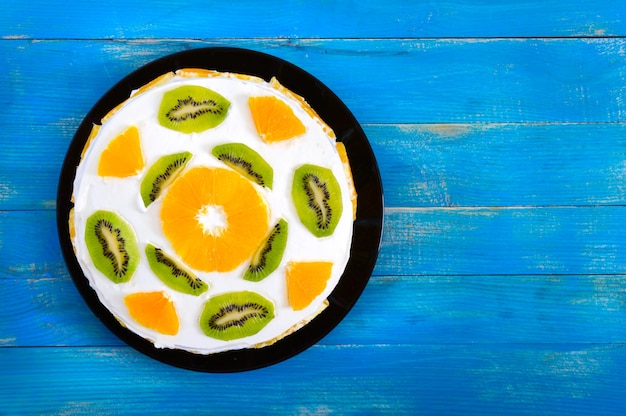 Bella torta di frutta su uno sfondo di legno blu. Torta festiva con arance, kiwi. Vista dall'alto. Buon compleanno.