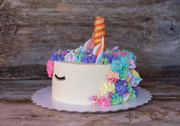 Bella torta fatta in casa a forma di unicorno con fiori color crema su un tavolo di legno