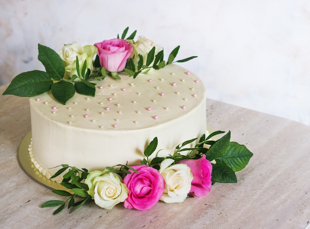 Bella torta nunziale con i fiori sulla tavola di marmo e sulla superficie bianca