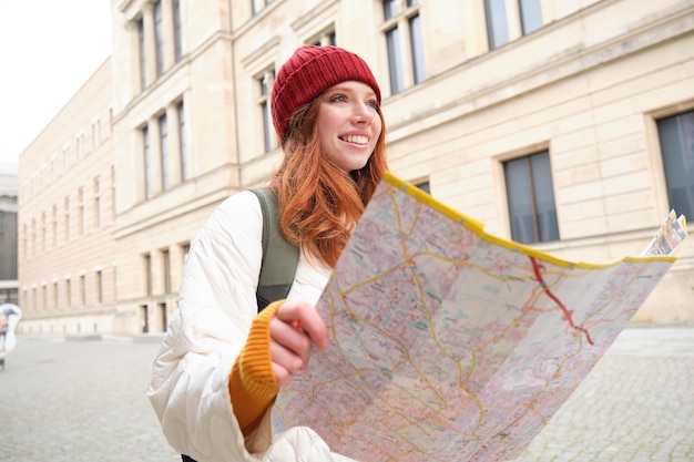 Bella turista rossa con mappa della città esplora il punto di riferimento storico che cammina intorno