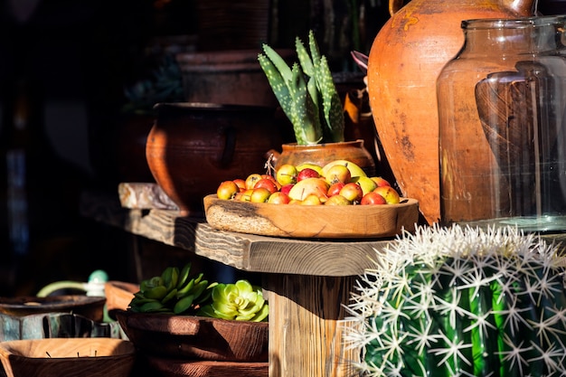 Bella vetrina nel mercato della frutta con mele rosse su un vassoio di legno, cactus e vasi di argilla