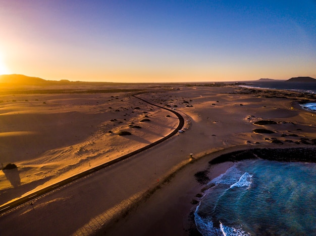 Bella vista aerea della spiaggia costiera durante il tramonto - oceano blu e sabbia gialla e deserto con luce solare provengono dalle montagne