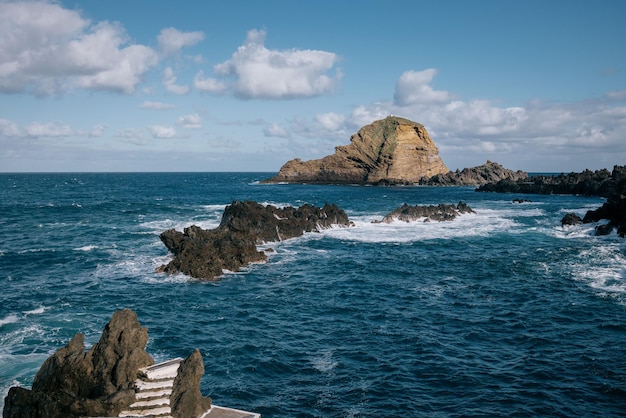 Bella vista del mare ondulato e delle enormi rocce dalla piscina naturale di Porto Moniz sotto un cielo blu