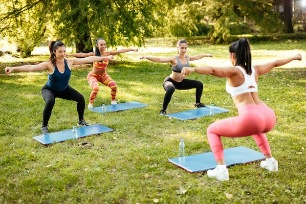 Belle amiche che fanno esercizi di squat nel parco con un istruttore di fitness femminile.