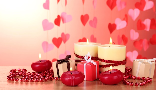 Belle candele con decorazioni romantiche su un tavolo di legno su sfondo rosso