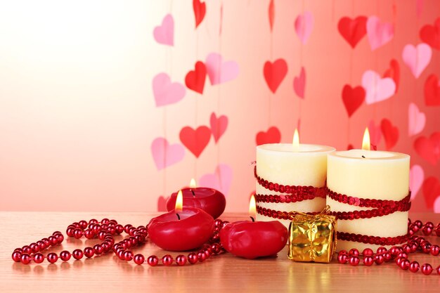Belle candele con decorazioni romantiche su un tavolo di legno su sfondo rosso