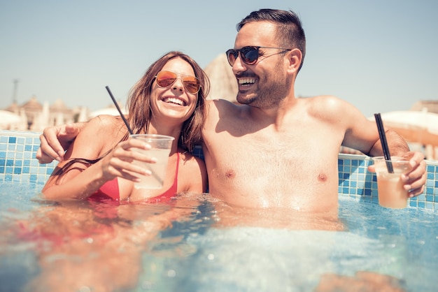 Belle coppie che bevono cocktail in piscina