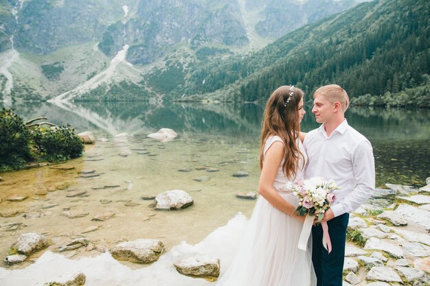 Belle coppie moderne vicino a un lago in montagna fanno foto di matrimonio