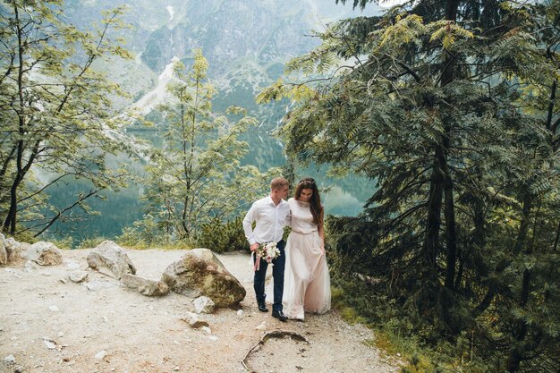 Belle coppie moderne vicino a un lago in montagna fanno foto di matrimonio