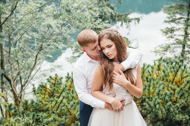 Belle coppie moderne vicino a un lago in montagna fanno foto di matrimonio