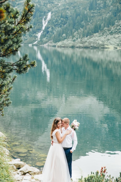 Belle coppie moderne vicino a un lago in montagna fanno foto di matrimonio