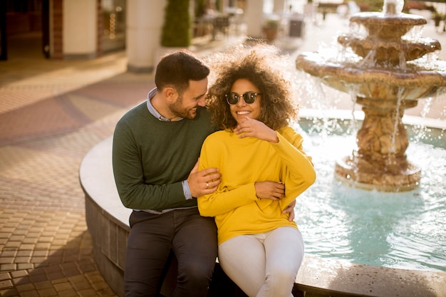 Belle coppie sorridenti di amore che si siedono vicino alla fontana un giorno soleggiato