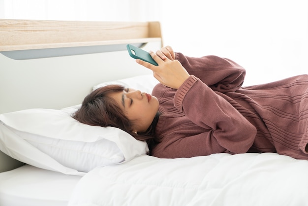 belle donne asiatiche che giocano smartphone sul letto