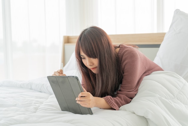 belle donne asiatiche che lavorano con tablet sul letto