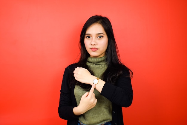 belle donne asiatiche che usano un maglione nero che puntano all'orologio con sfondo rosso isolato