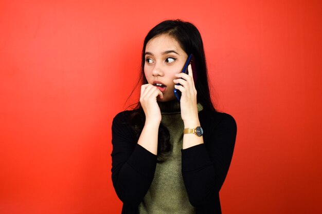 Belle donne asiatiche che usano un maglione nero scioccanti e parlano al telefono cellulare isolato su rosso