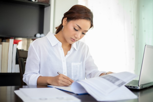 Belle donne asiatiche di affari che controllano documento e che per mezzo del taccuino per lavorare a casa