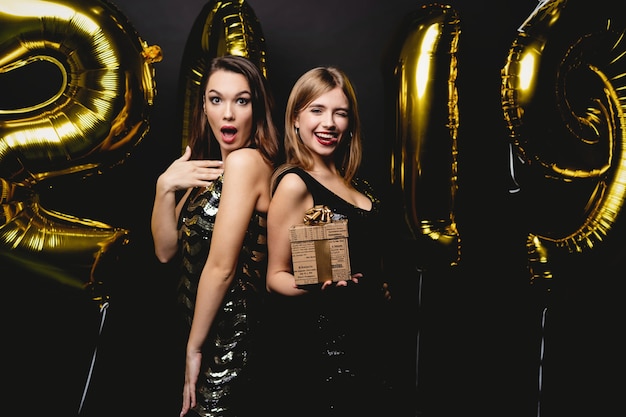 Belle donne che celebrano il nuovo anno. Felice bellissime ragazze in abiti da festa sexy alla moda che tengono palloncini d'oro 2019, divertirsi alla festa di Capodanno. Celebrazione delle vacanze. Immagine di alta qualità