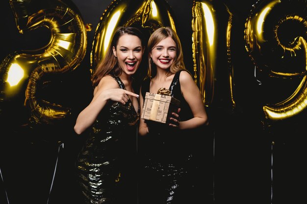 Belle donne che celebrano il nuovo anno. Felice bellissime ragazze in abiti da festa sexy alla moda che tengono palloncini d'oro 2019, divertirsi alla festa di Capodanno. Celebrazione delle vacanze. Immagine di alta qualità